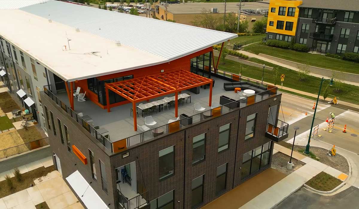 Drone aerial video of Sona Lofts showing the full residential building, rooftop, parking area, and surrounding streetscape.