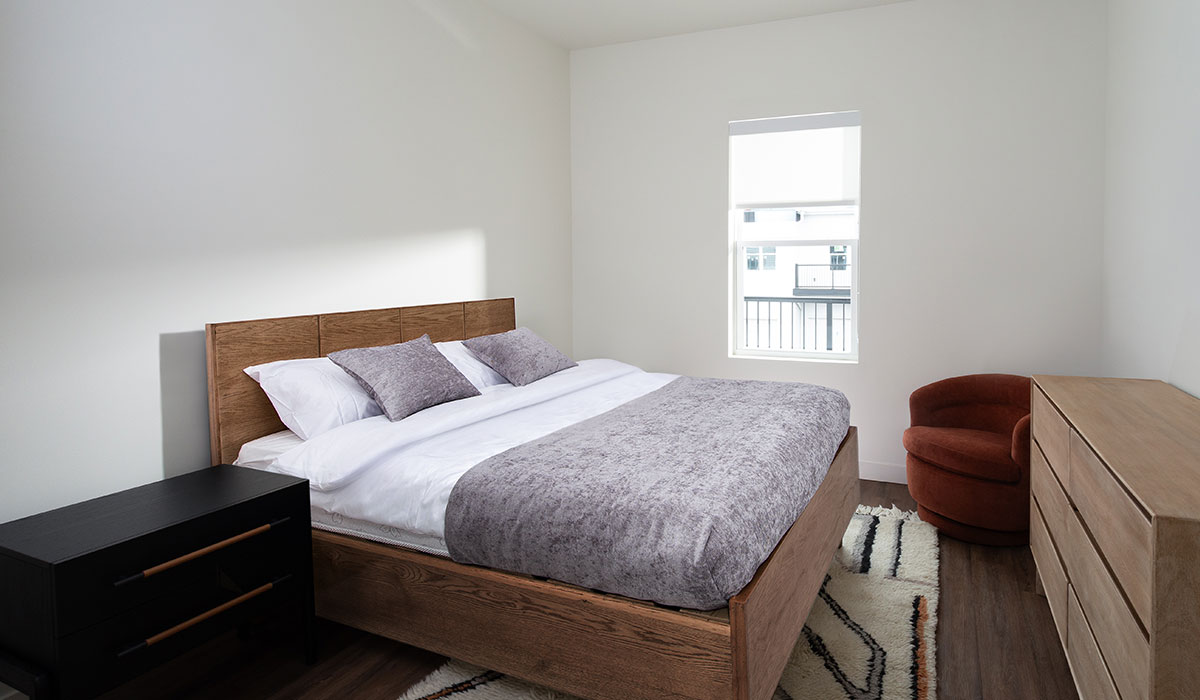 Contemporary Bedroom at Emree Apartments in Wisconsin Bright and modern bedroom at Emree Apartments with large window, neutral decor, and cozy furnishings